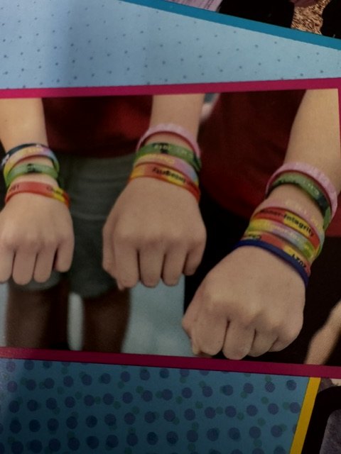 Close photograph of four wrists stacked with many colored rubber C.H.I. wristbands, from a scrapbook page.